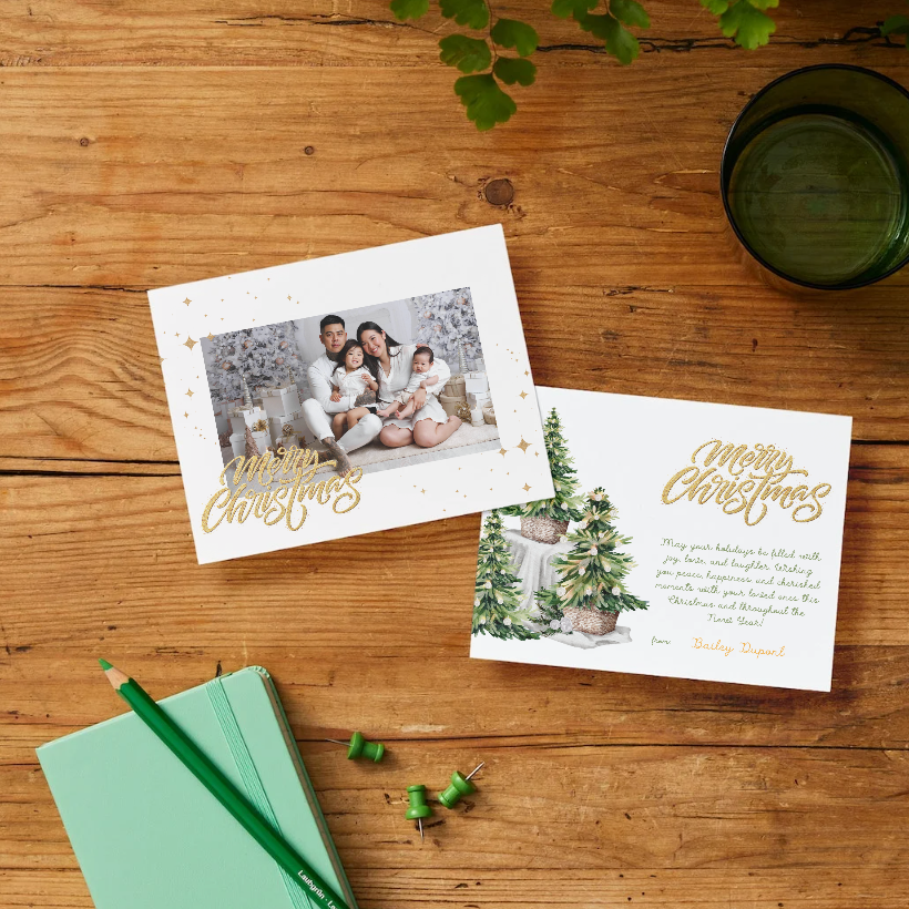 Two Christmas cards on a wooden surface with a notebook and pencil.